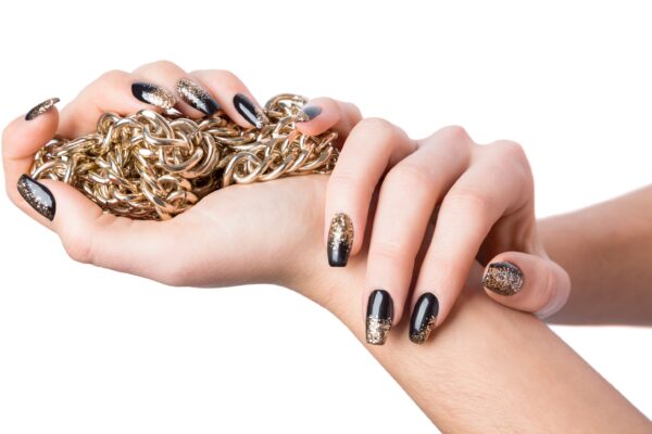 Close up of stylish hands painted black and glittery gold against a white background near shiny chain necklace